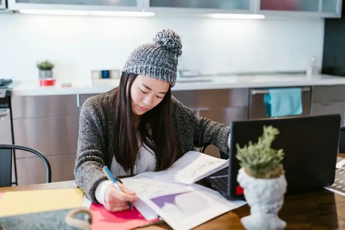 Woman sitting in front of a laptop and reviewing content on paper.