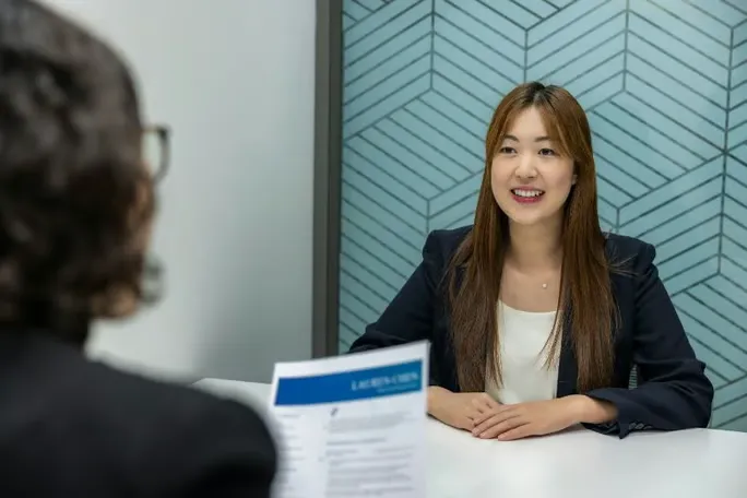 A woman sits at a table smiling during a job interview.