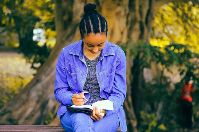 Woman writing in a journal while sitting on a park bench.