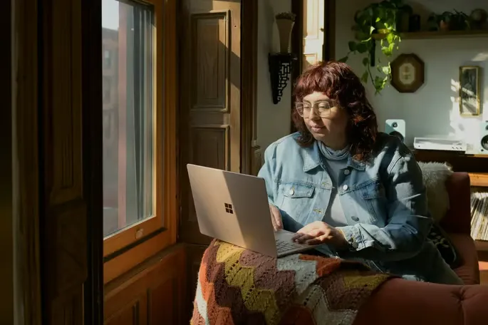 Woman using ChatGPT tool on computer sitting by window.