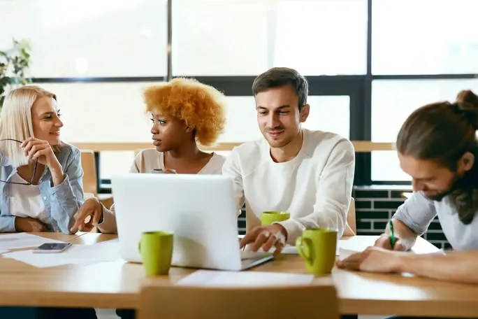 Four coworkers sitting at a table using an AI text humanizer tool on the computer.