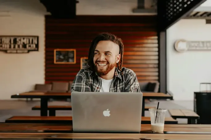 Man in plaid shirt smiling while working on computer.