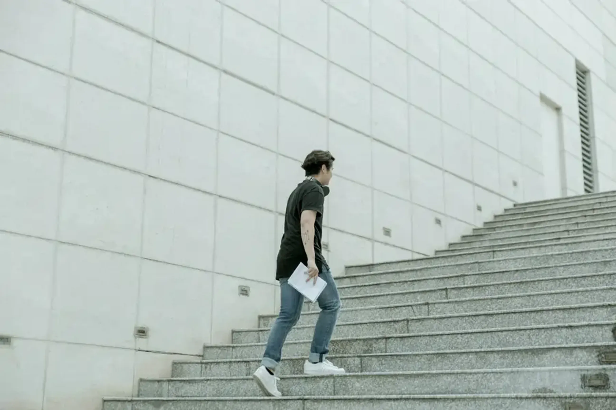 Man walking up outdoor stairs holding papers.