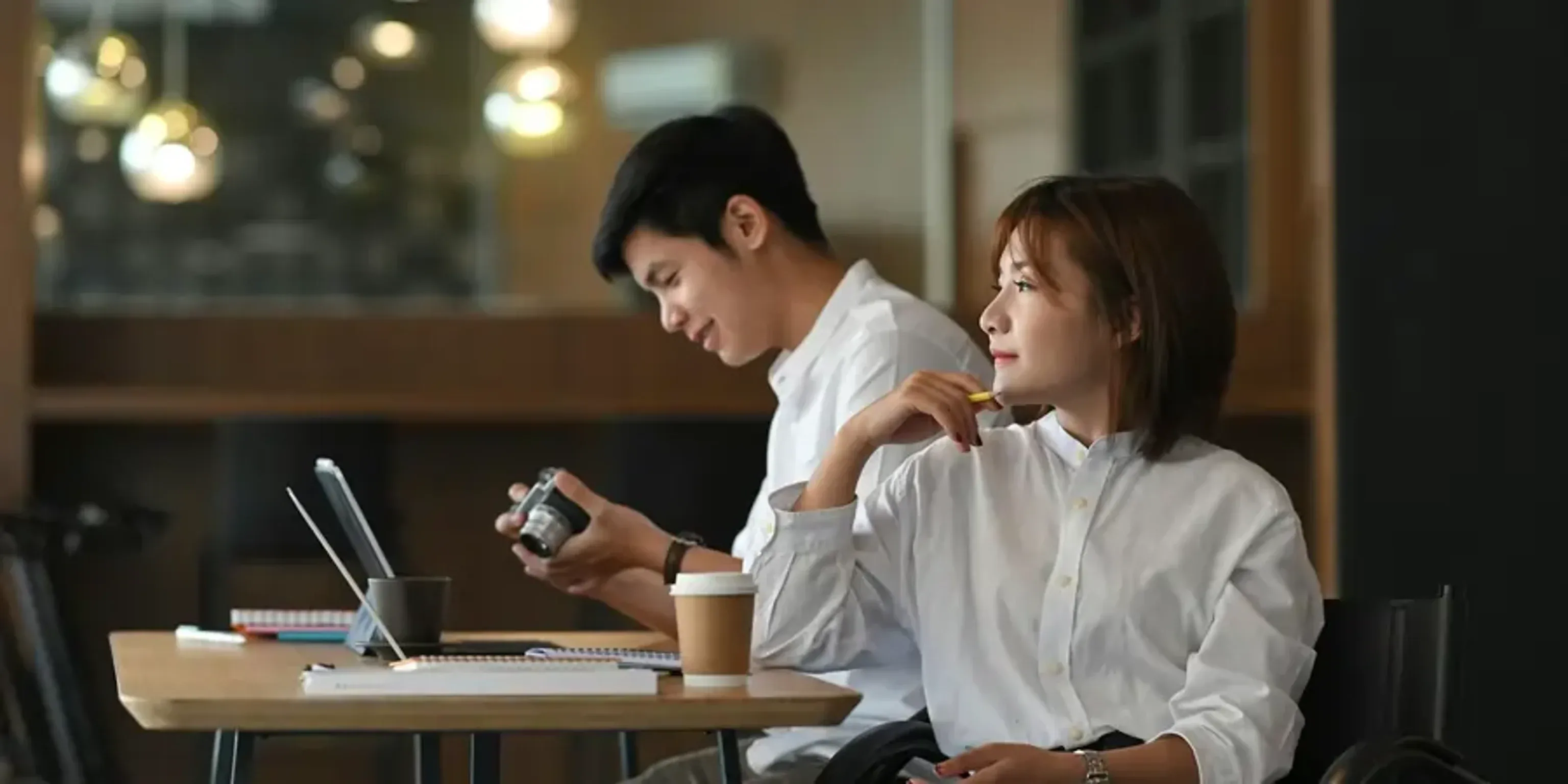 Two coworkers sitting at a table working with a laptop and camera.