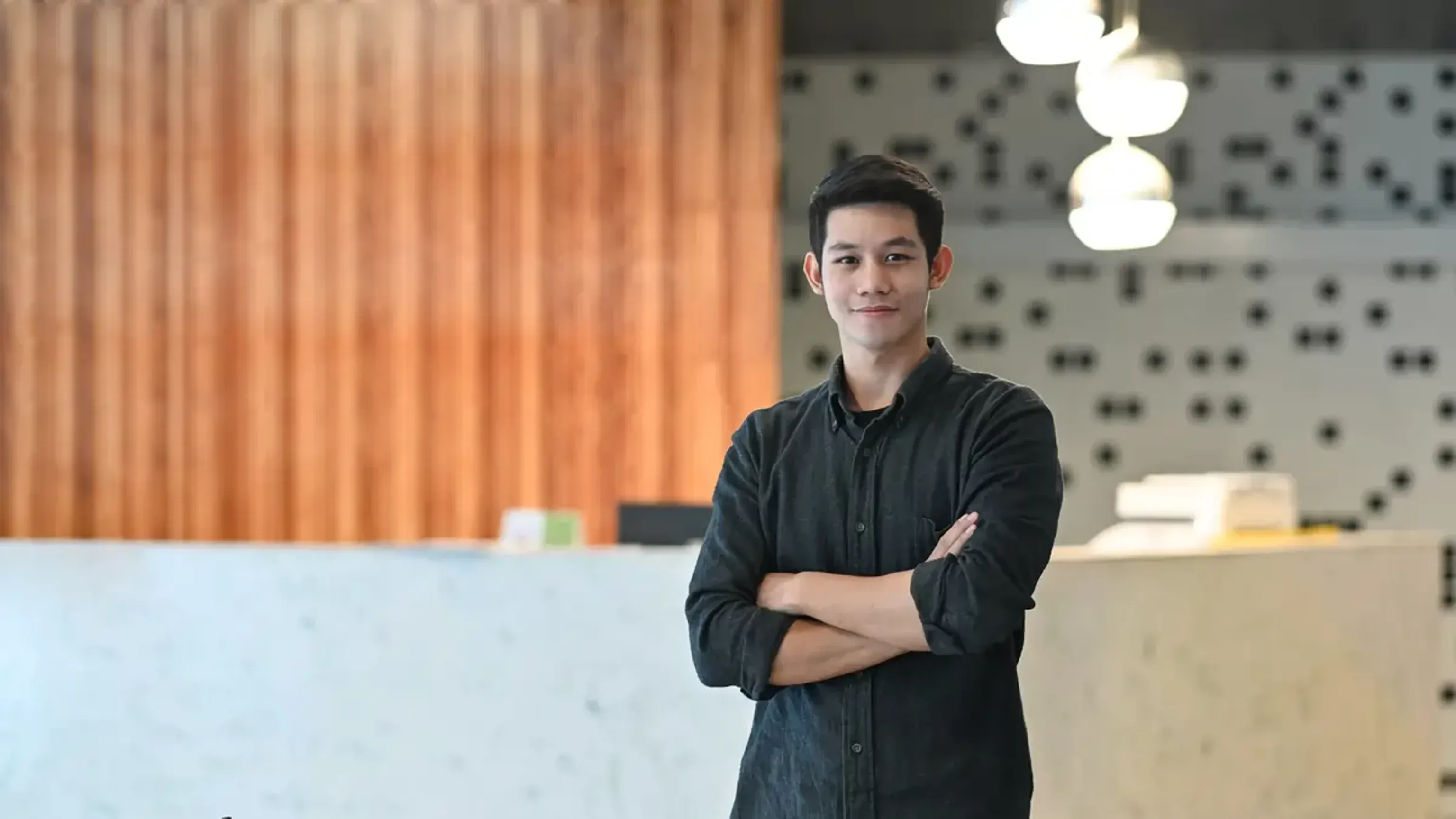 Young man standing with arms crossed in a modern office lobby.